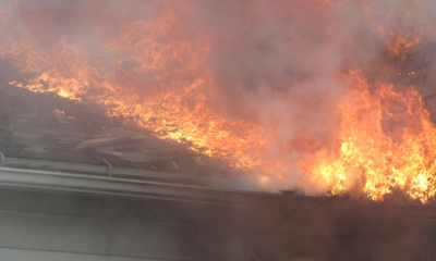 Des flammes vives illuminent une maison en feu, projetant un panache de fumée dans le ciel