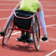 An athlete in a racing wheelchair waits at the starting line of a racetrack.